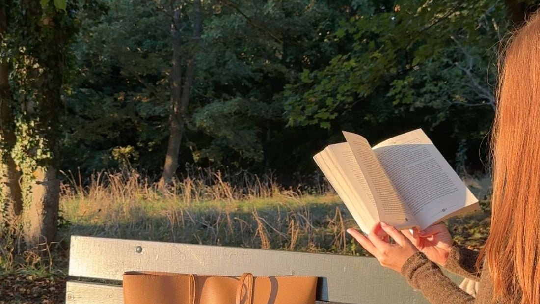 Frau mit langen roten Haaren liest im herbstlichen Abendlicht auf einer Parkbank