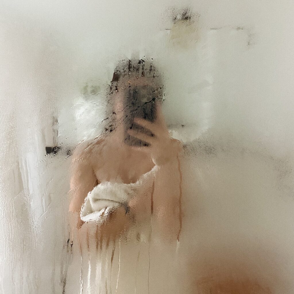 Frau nach der Dusche im beschlagenen Badezimmerspiegel – bewusstes Körperpflegemoment